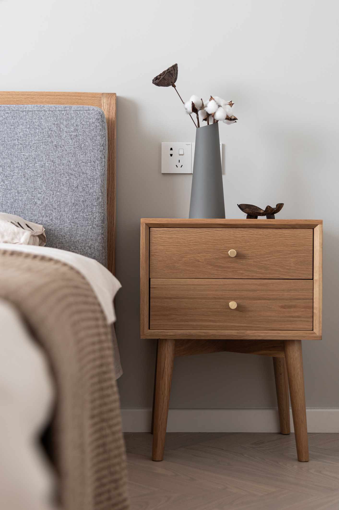 Table de chevet en bois avec un vase et un petit bol à côté d'un lit