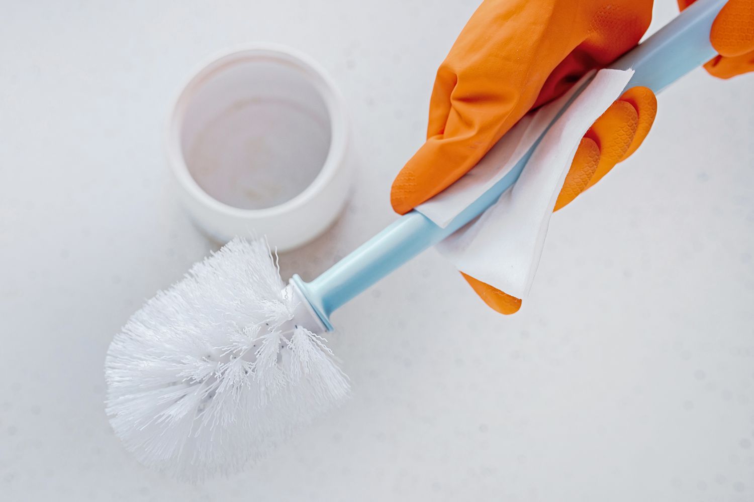 Personne essuyant le manche d'une brosse de toilette avec une lingette désinfectante