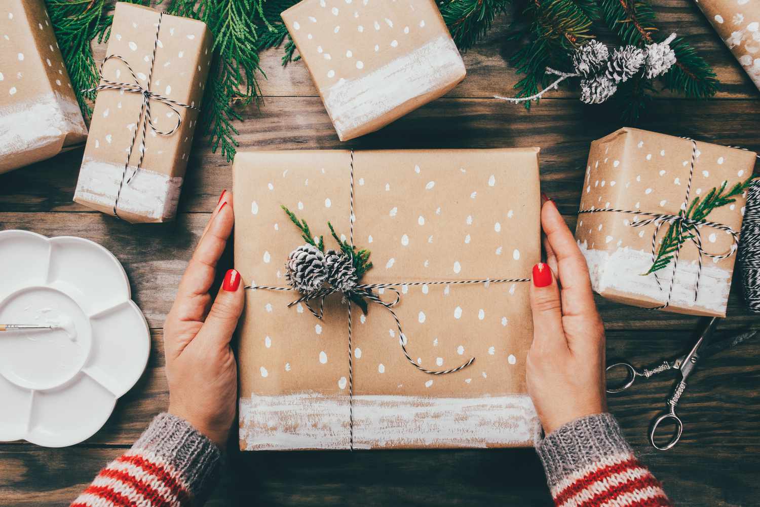 Personne tenant un cadeau emballé dans du papier Kraft décoré de peinture blanche